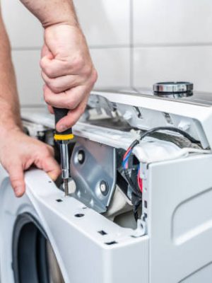 Repairman using a screwdriver disassembles a washing machine for repair
